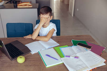 Lazy sad little boy pupil closing his eyes with hand. A lot of difficult homework.