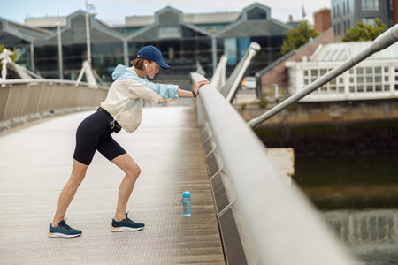 Sportive woman doing stretching exercise on footbridge at morning in the city