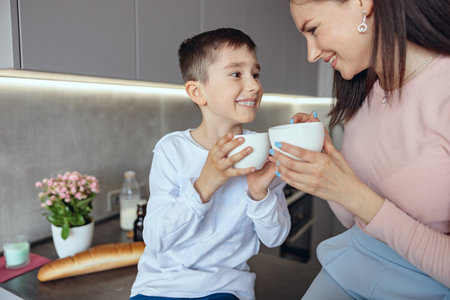 Pretty mom and little teen son holding cups and looking at each other with smile and love.の写真素材