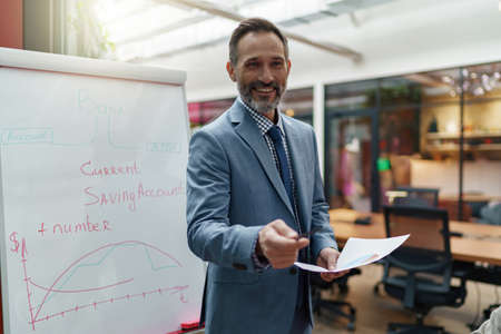 Mature business coach or speaker make flip chart presentation to diverse businesspeople at meetingの写真素材