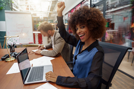 Happy african businesswoman sitting on his workplace in modern office on colleague backgroundの写真素材