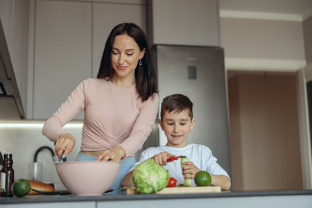 Portrait shot of beautiful mother cooking and cute son helping to peel vegetables.の写真素材