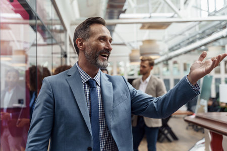 Mature smiling businessman standing in office on colleagues background and waving hi
