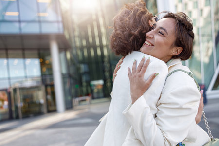 Two emotional happy woman friends in trendy outfits hugging each other on city streetの写真素材
