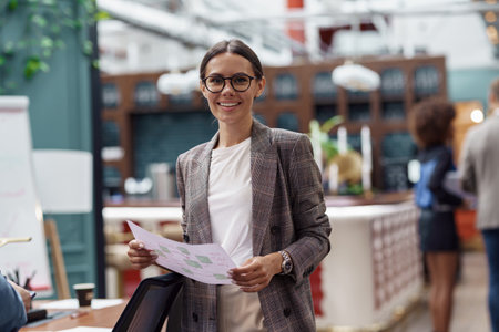 Portrait of smiling businesswoman standing in modern office on colleagues backgroundの写真素材