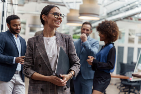 Portrait of smiling businesswoman in glasses standing in modern office on colleagues backgroundの写真素材