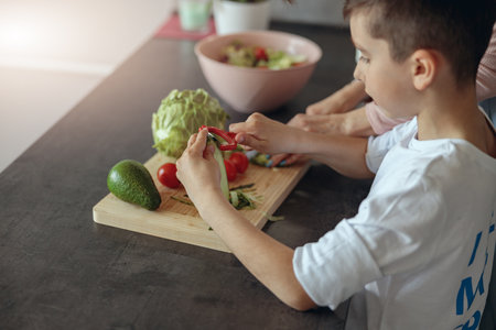 Close up of small teen Caucasian boy peeling cucumber. Mom teaching son to cook.の写真素材