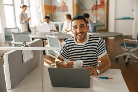 Smiling Businessman working laptop while sitting in modern office on colleagues backgroundの写真素材