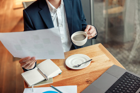 Close up of unrecognisable businessman drinking coffee and working with documents in cafeの写真素材