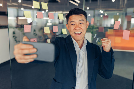 Happy Asian businessman taking selfie in office during working dayの写真素材