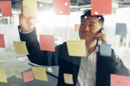 Businessman writing on sticky notes on glass wall while working in modern officeの写真素材