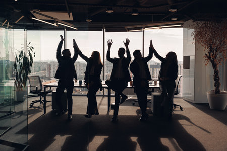 Silhouette photo of business people with raised hands while standing in meeting roomの写真素材