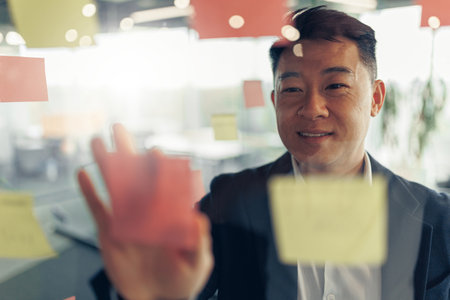 Close up of asian businessman is glues sticky notes on motivation board in modern officeの写真素材