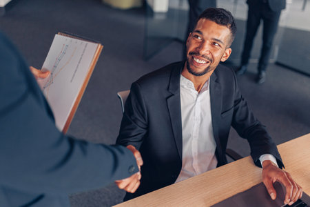 Two multiracial colleagues shaking hands during working day in office