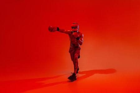 Sporty man wearing head guard and boxing gloves practicing for fight on studio backgroundの写真素材