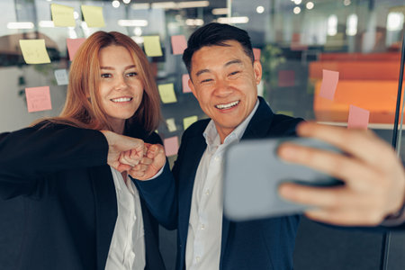Two multi ethnic business colleagues taking selfie while standing in modern officeの写真素材
