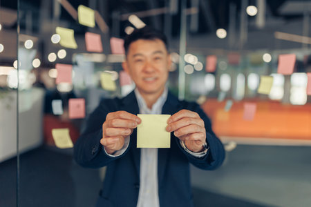 Asian Businessman showing empty sticky notes while standing in modern officeの写真素材