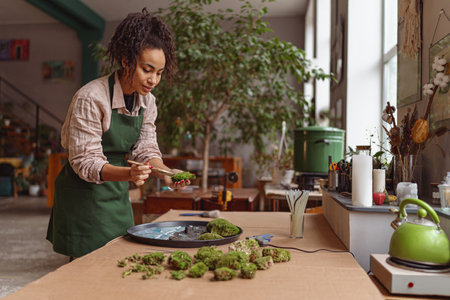 Professional woman decorator making green ikebana on tray with epoxy resin in florist workshop
