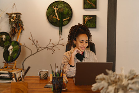 Smiling female florist working on laptop in floral studio, check customers order