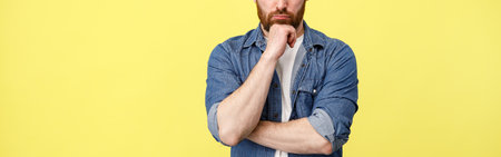 Serious man houghtfully hold hand near beard in yellow backgroundの写真素材