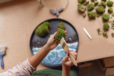 Top view of woman decorator making green ikebana on tray with epoxy resin in florist workshopの写真素材