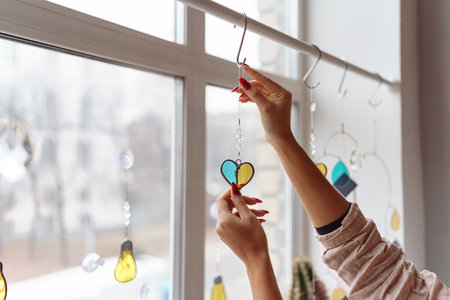 Woman hands decorate window with glass decoration in the form of a heartの写真素材