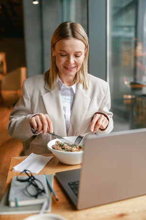 Cheerful businesswoman is having a business lunch and working on laptop in cafe. Blurred background