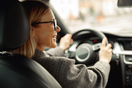 Rear view of smiling woman driving car and holding both hands on steering wheel on the way to workの写真素材