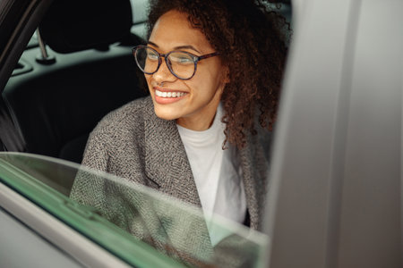 Smiling young woman office worker wearing glasses sit in city taxi and looking at window