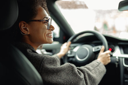 Smiling businesswoman driving car and holding both hands on steering wheel on the way to workの写真素材