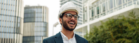 Indian construction architect in suit and hardhat with paper folder in hands against modern building