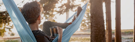 Rear of young man traveler lying and resting in hammock with hot drink in forest. Travel.の写真素材