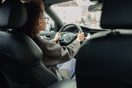 Rear view of woman driving car and holding both hands on steering wheel on the way to workの写真素材