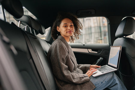 Smiling businesswoman analyst working on laptop sitting car leather backseat on way to officeの写真素材