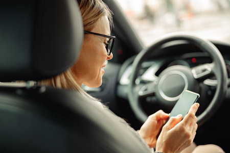 Side view of woman driver in eyeglasses is using phone while sitting behind steering wheel in car