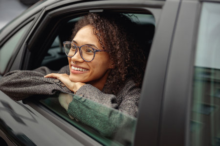 Smiling young woman office worker wearing glasses sit in city taxi and looking at window