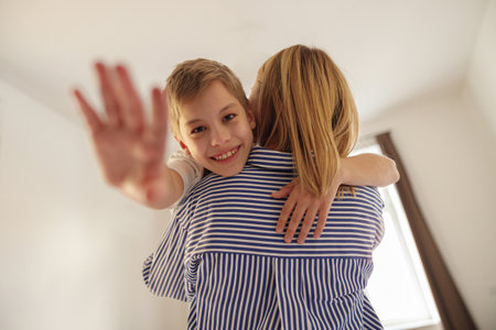 Back view of mom spends time with smiling son, holding him in her arms and hugging tenderlyの写真素材