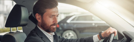 Handsome businessman in grey suit is riding behind steering wheel of car and turns on musicの写真素材