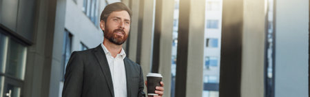 Attractive european businessman with coffee and laptop near office building during breakの写真素材
