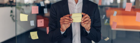 African Businessman showing sticky notes with motivational phrases while standing in officeの写真素材