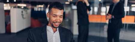 Smiling african businessman working laptop in modern office on colleagues backgroundの写真素材