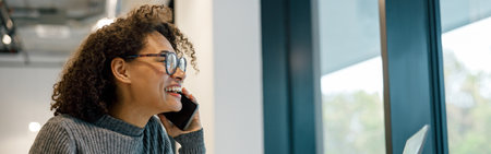 Smiling woman freelancer working laptop and talking phone while sitting in cozy coworking