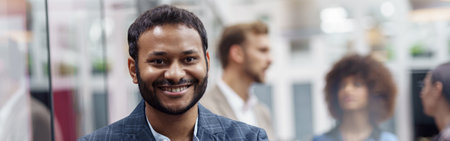 Portrait of indian businessman standing in modern office on colleagues background