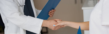 Close up of two doctors in uniform shaking hands standing in clinic hall near receptionの写真素材