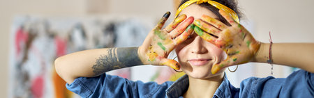 Portrait of creative woman holding her hands in paint over her eyes while creating abstract painting at home studio workshopの写真素材