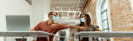 Students siting and greeting bumping elbows at workplaceの写真素材