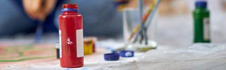 Close up shot of red acrylic paint in jar. Woman working on painting in the background. Oil paintsの写真素材