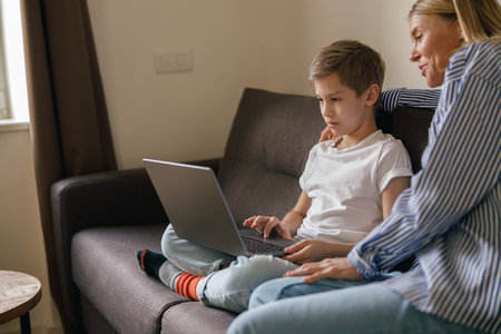 Mom and son looking for something on the web, games and curious newswhile sitting on sofaの写真素材