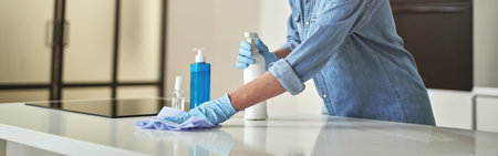 Happy mature woman in rubber gloves smiling at camera, using detergent spray and cloth while cleaning surface in the kitchenの写真素材