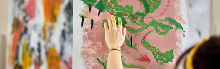 Close up shot of hand of female artist applying paint on canvas with fingers while creating abstract painting at home studio workshopの写真素材